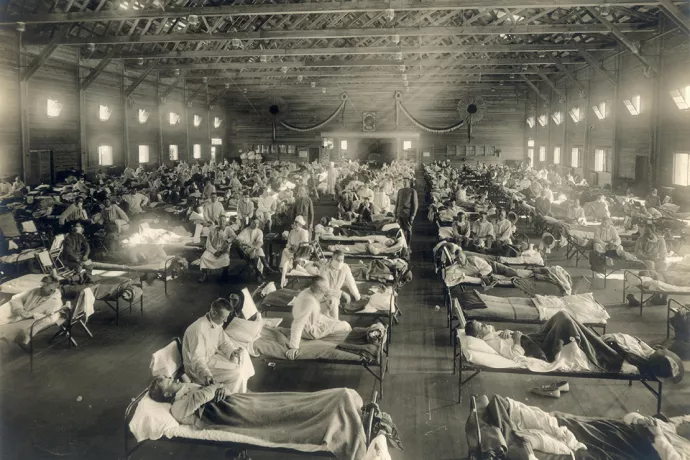 Seven rows of beds in a large, open building, occupied by men wearing masks.