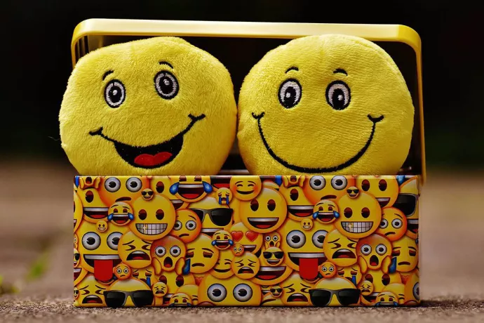Two smiling emoji plush toys in a box covered in emoji art