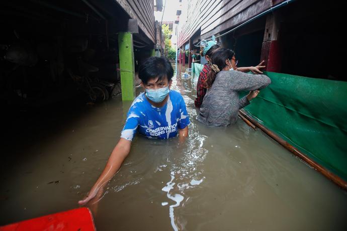 A man wearing a blue shirt and blue surgical face masks walks toward the camera in chest-high flood waters.rrow alley.