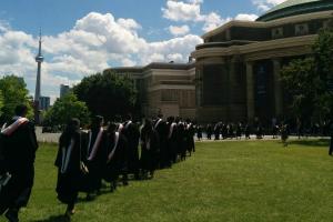 people in graduation gowns walk across a lawn