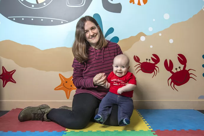Laura Cirelli sitting in front of a colourful wall mural with starfish and crabs holding her son Ian