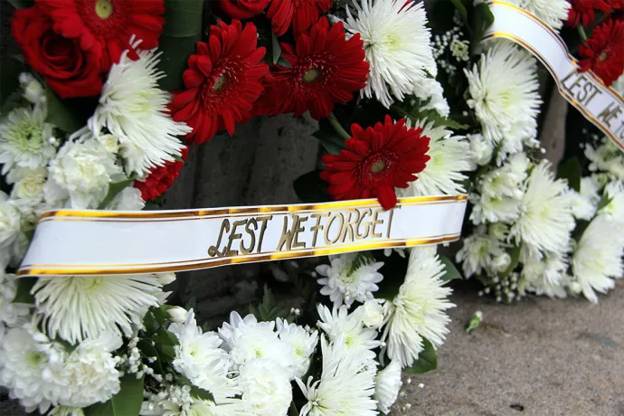 Close up of wreath with red and white flowers and banner that reads "lest we forget"