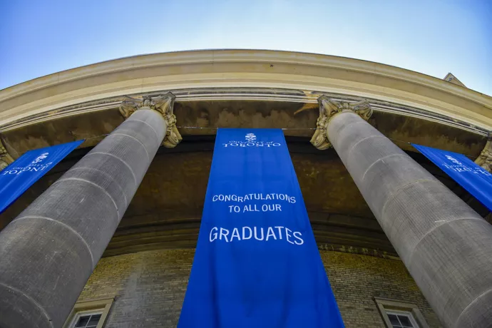 Looking up at convocation hall columns outside, blue banner reads: University of Toronto. Congratulations to all our graduates.