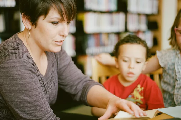 Woman helping a young boy read a book