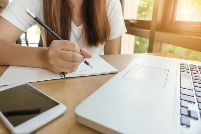 Woman holding pencil over open notebook with open laptop on front of her