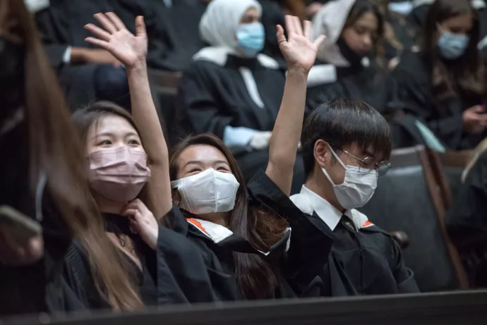 a student in a mask raises her hands in celebration inside Convocation Hall