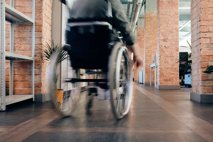 Individual in wheelchair moving away from camera in hallway with brick pillars on either side