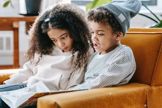 Two children sitting on couch reading a book together