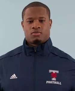 photo of a man with brown skin, short hair and a navy blue windbreaker