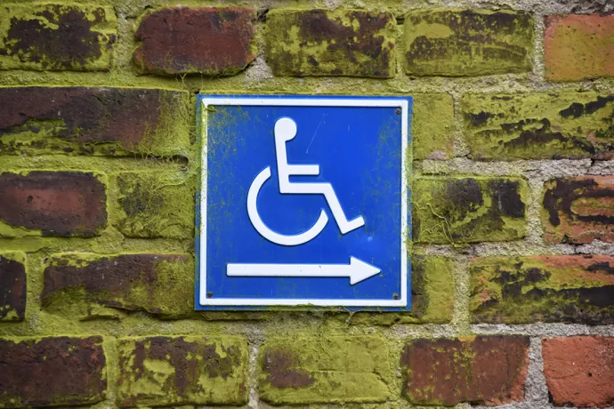 Brick wall with blue sign with white line drawing of wheelchair and an arrow pointing right