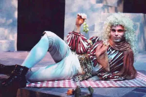 actor wearing a white french wig reclines on a stage