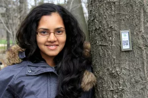 woman with long dark hair smiling and leaning against a tree trunk