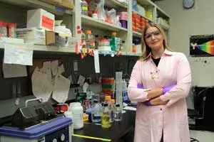 Sasha Weiditch wears a pink lab coat and stands beside her lab bench.