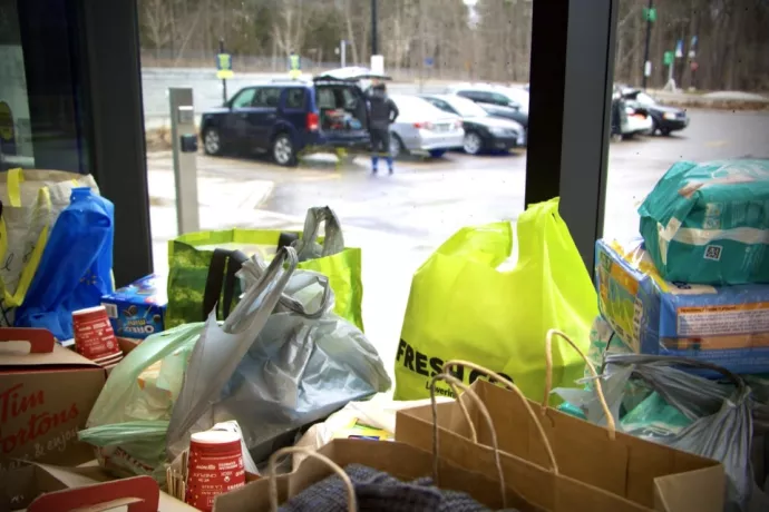 Donations of groceries and diapers are piled up in bags on a table