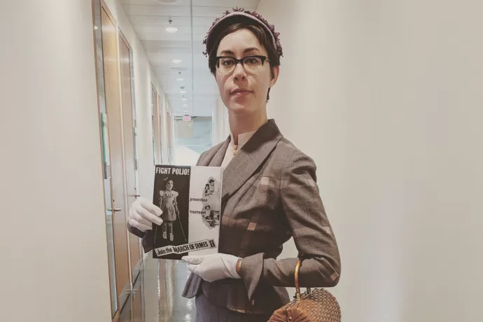 Madeleine Mant wears a vintage suit from the 1950s and holds a pamphlet advertising polio vaccines.