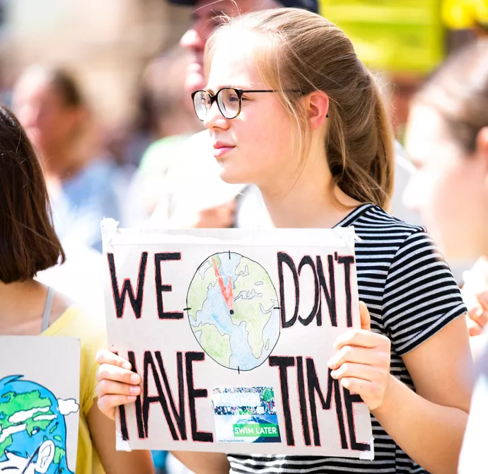 Girl holding protest sign with earth painted on it and words we don't have time