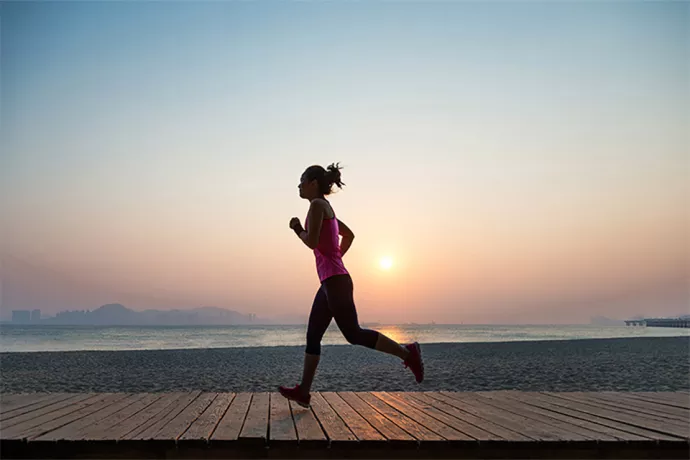 Woman running along a beach, sun rising behind her over the water
