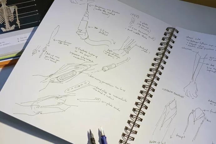 Open sketch book with sketches of unidentified surgical tools and arms