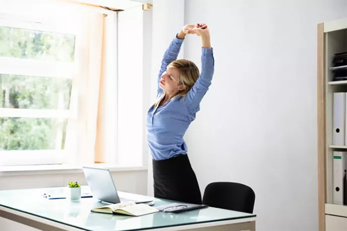 Woman standing and stretching in front of her desk