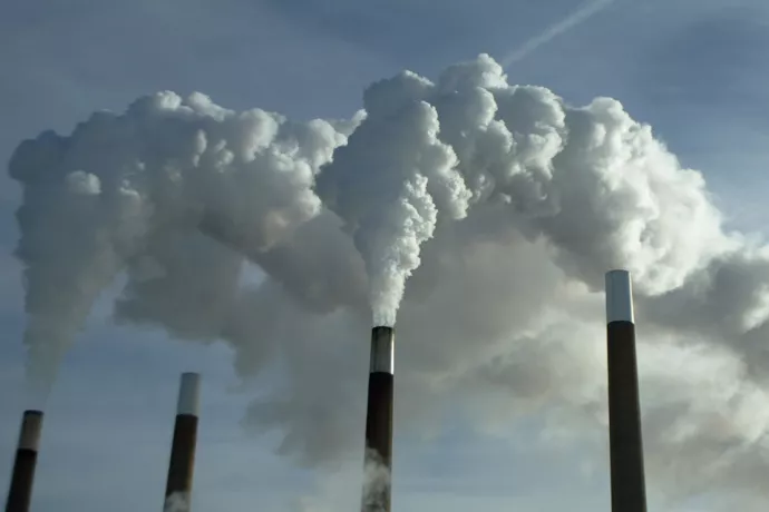 Three smoke stacks spewing white clouds it steam into the clear blue sky