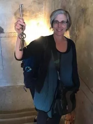 Jill Caskey standing in an old stairwell holding up a large old iron key