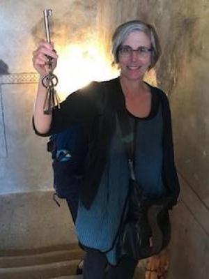 Jill Caskey standing in an old stairwell holding up a large old iron key