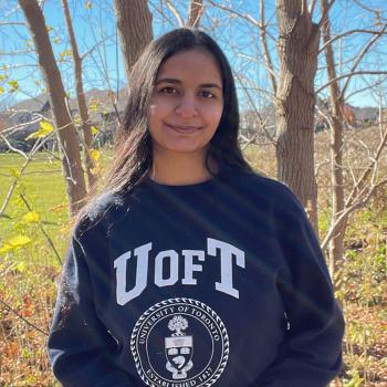 Neha Sharma stands in front of a tree wearing a UofT sweater.