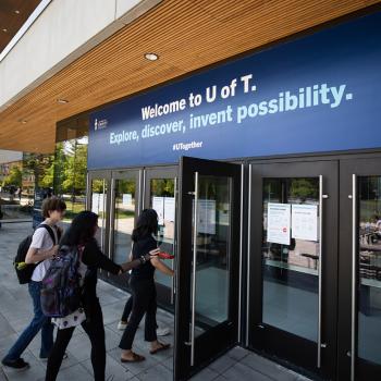 Students walking through glass doors with sign above doors that reads Welcome to U of T. Explore, discover, invent possibility