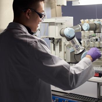 Researcher in white lab coat and gloves works on task in a lab
