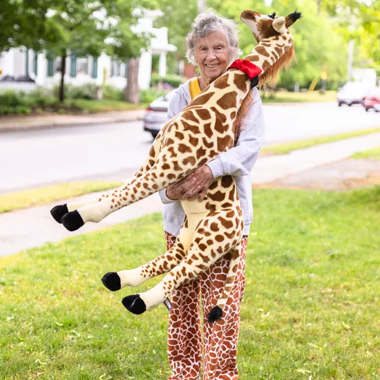 Anne Innis Dagg standing on a lawn wearing giraffe-print pants holding a large stuffed giraffe