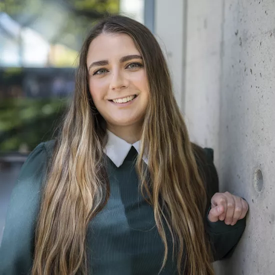 Ashley Pozzo, a UTM student with long hair and wearing a dark green shirt, smiles at the camera. 