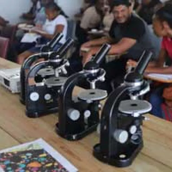 Close-up photo of three microscopes on a table with students in the background