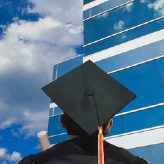 man in mortar board hat looking at tall building with blue sky in background
