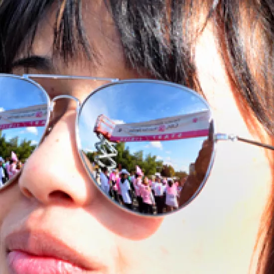 Run for the Cure banner and balloons reflected in woman's sunglasses