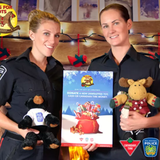 Peel Police constables hold stuffed animals in front of Toys for Tots logo