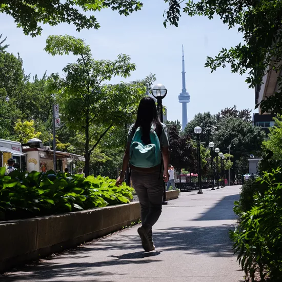 female student with backpack walking along sidewalk with CN Tower in background