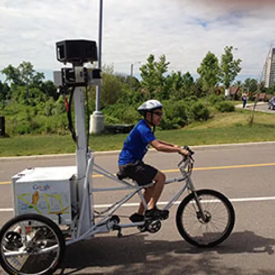 A smiling man pedals, pulling a large camera mounted to a post on a specialized bike used to capture images for Google Street View