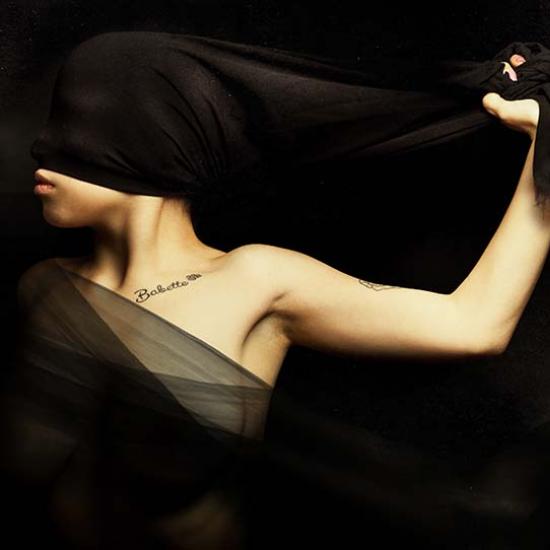 Artistic photo of woman holding a sheer black sash with a tattoo on her lower neck