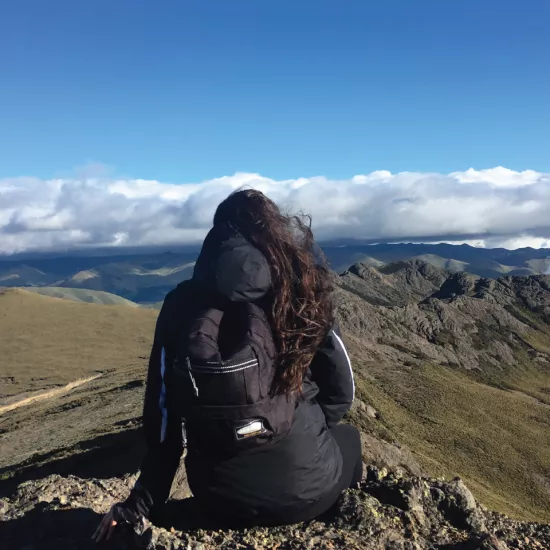 Student sitting on mountainside looking at horizon