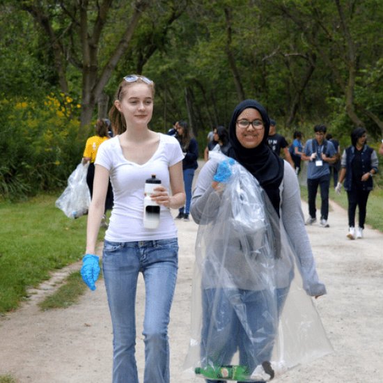 2 students at river clean up event. Student on right is holding a garbage bag.