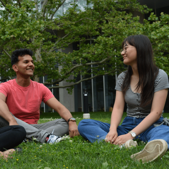 2 students sitting outside on the grass.