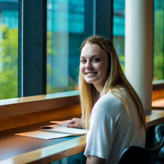 A student smiling at a desk in front of a window.