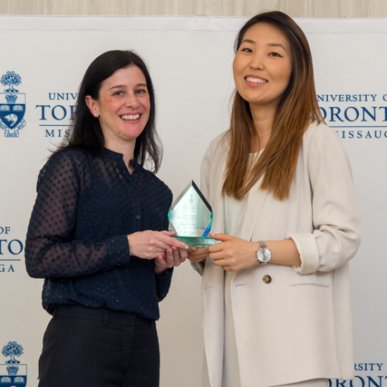 A faculty member and student holding an award, smiling.