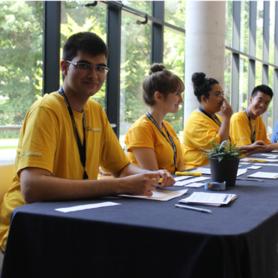 4 students in yellow shirts sitting at a registration table.