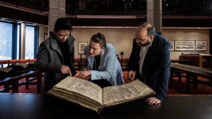 Alex Gillespie and research peers looking at an ancient manuscript in the Fisher Library