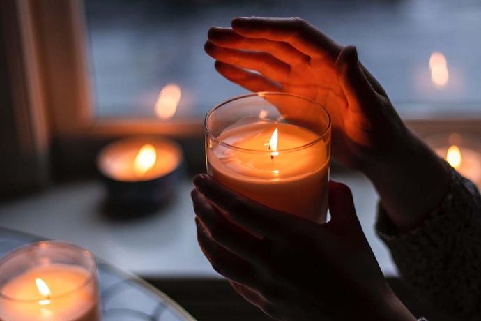 Hand holding a lit candle, with other lit candles in the background