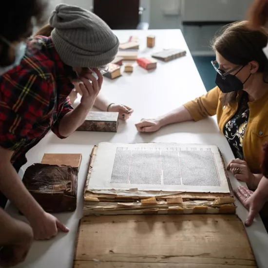 People look at large manuscripts on a wooden table