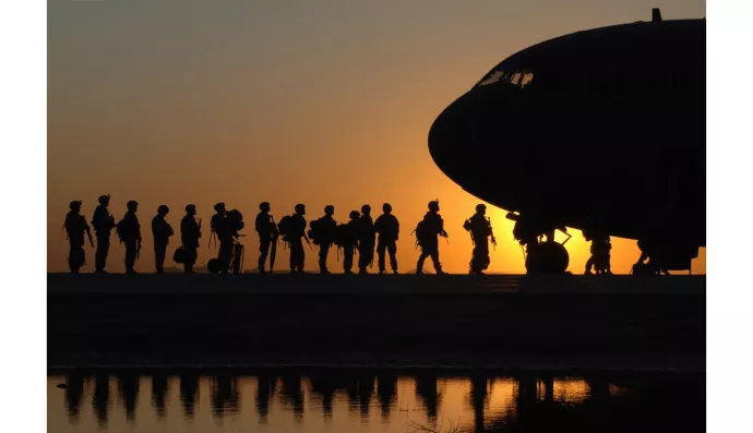silhouette of soldiers boarding a military plane against a setting sun