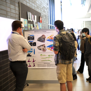Two male students stand with their backs to the camera as they look thoughtfully at a poster.